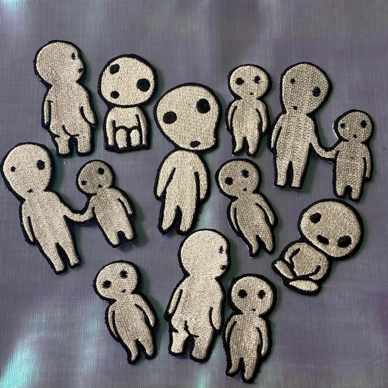 May include: A collection of twelve embroidered patches featuring stylized white figures with large round heads and black circular eyes. The figures are depicted in various poses, including standing, sitting, and holding hands, all outlined in black thread.
