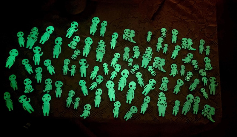 May include: A large collection of small, glow-in-the-dark figurines shaped like stylized forest spirits. Each figure features a smooth, rounded head with large, hollow eyes and a simple body, emitting a bright, neon green light in the darkness.