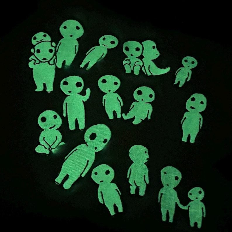 May include: A collection of small, glow-in-the-dark figures shaped like stylized forest spirits. The figures are light green and emit a bright luminescence against a dark background, featuring various poses including standing, sitting, and pairs.