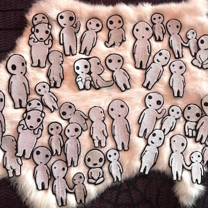 May include: A collection of numerous small, white, embroidered patches featuring stylized, round-headed figures with simple black facial features. The patches depict various poses, including standing, sitting, and holding hands, with a textured fabric finish.