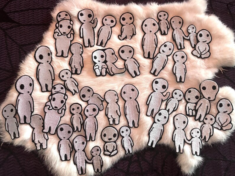 May include: A collection of numerous small, white, embroidered patches featuring stylized, round-headed figures with simple black facial features. The patches depict various poses, including standing, sitting, and holding hands, with a textured fabric finish.