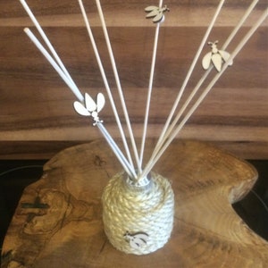 May include: A natural reed diffuser with a rope-wrapped bottle and wooden bee accents. The diffuser is on a wooden surface.