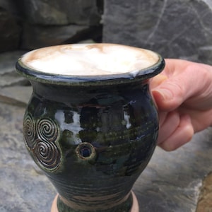 May include: A green ceramic mug with a brown swirl design and a beige base, filled with a light brown beverage topped with foam.