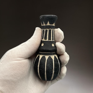 Pode incluir: Um pequeno vaso de cerâmica preto e branco com corpo bulboso e pescoço estreito. O vaso tem um desenho geométrico.