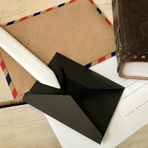 May include: A white paper letter opener with a black envelope on a white sheet of paper with a brown envelope with red and blue stripes in the background.