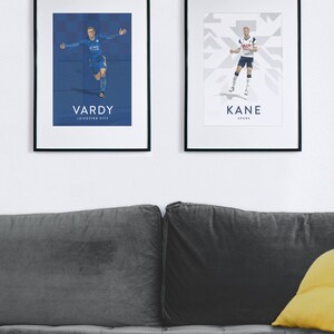 Pode incluir: Dois cartazes emoldurados de jogadores de futebol profissionais. O cartaz &agrave; esquerda apresenta Jamie Vardy com um uniforme de futebol azul com o texto "VARDY LEICESTER CITY". O cartaz &agrave; direita apresenta Harry Kane com um uniforme de futebol branco com o texto "KANE SPURS".
