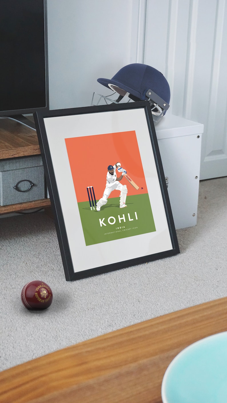 Pode incluir: Uma impress&atilde;o emoldurada de um jogador de cr&iacute;quete em a&ccedil;&atilde;o. O jogador est&aacute; vestindo um uniforme branco e um capacete. A impress&atilde;o tem um fundo vermelho e grama verde. O texto "KOHLI INDIA INTERNATIONAL CRICKET ICON" &eacute; impresso abaixo do jogador.