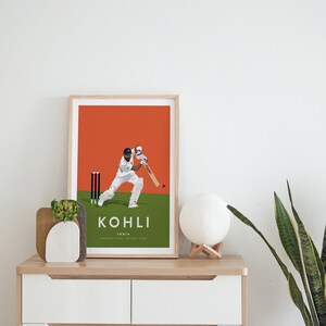 Pode incluir: Uma impress&atilde;o emoldurada de um jogador de cr&iacute;quete em a&ccedil;&atilde;o, com fundo laranja, grama verde e o texto "KOHLI INDIA INTERNATIONAL CRICKET ICON".