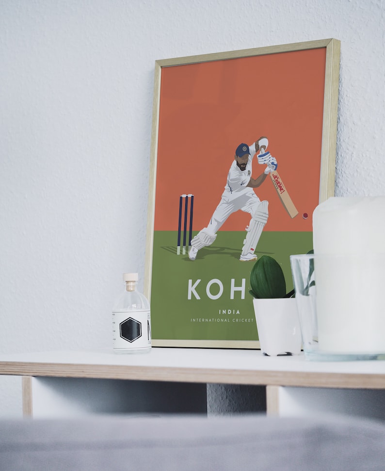 Pode incluir: Um p&ocirc;ster emoldurado com uma ilustra&ccedil;&atilde;o gr&aacute;fica de um jogador de cr&iacute;quete em a&ccedil;&atilde;o. O jogador est&aacute; vestindo um uniforme branco e um bon&eacute; azul. O p&ocirc;ster tem um fundo verde com um wicket de cr&iacute;quete e o texto "KOHLI INDIA INTERNATIONAL CRICKET".