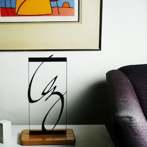 May include: A black metal sculpture of an abstract design, with a curved line and a circle, on a wooden base.