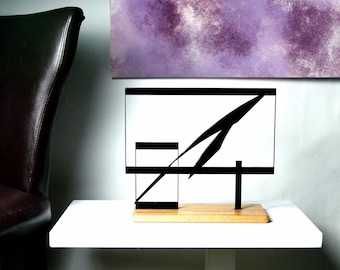 May include: A black metal sculpture with geometric shapes and a wooden base. The sculpture is on a white shelf.