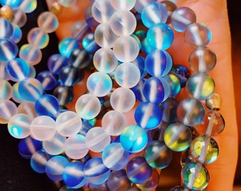 Könnte beinhalten: Ein Set aus drei schillernden Armbändern mit mattierten Glasperlen in den Farben Weiß, Blau und Grau.