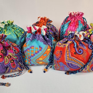 May include: A collection of colorful drawstring bags with vibrant patterns. The bags feature various designs, including paisley, geometric shapes, and floral motifs, in shades of red, purple, blue, and green. Each bag has a braided drawstring closure.
