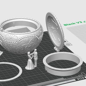 May include: A 3D printed model of a music box with a detailed design. The music box is open and the lid is separate. The music box is on a gray textured surface. The music box is made of white plastic. The music box is a wedding themed music box with a bride and groom figurine.
