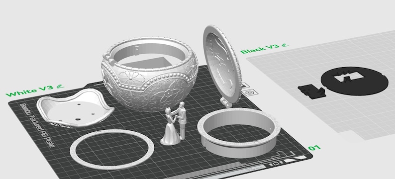 May include: A 3D printed model of a music box with a detailed design. The music box is open and the lid is separate. The music box is on a gray textured surface. The music box is made of white plastic. The music box is a wedding themed music box with a bride and groom figurine.