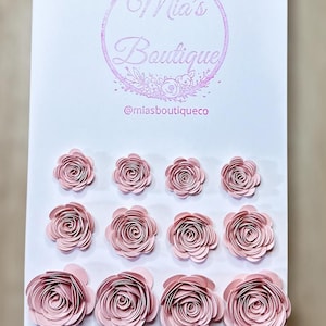 May include: A set of 10 pink paper flowers, arranged in rows on a white background. The flowers are all the same size and shape, and they have a delicate, layered look. The flowers are perfect for adding a touch of elegance to any craft project.