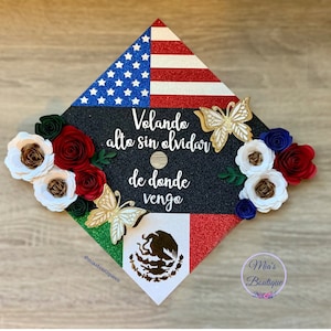 May include: Graduation cap decorated with red, white, and blue paper flowers, a gold butterfly, and the text "Volando alto sin olvidar de donde vengo" with the American and Mexican flags. The cap is black with glitter.