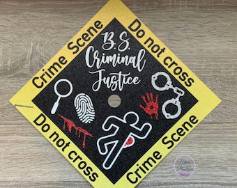 Puede incluir: Un gorro de graduación negro con ribete amarillo y purpurina. El gorro tiene una silueta blanca de una persona corriendo con una gota de sangre roja en el pecho. El texto en el gorro dice "Crime Scene Do not cross B.S. Criminal Justice Do not cross Crime Scene".