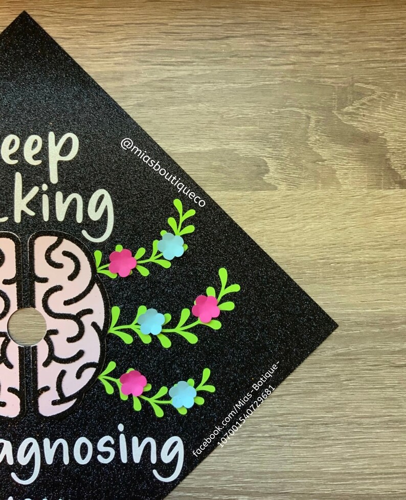 Op de afbeelding: Zwarte afstudeerhoed met glitter en een roze hersengrafiek. De tekst "Keep thinking" en "Diagnosing" staat op de hoed. De tekst "@miasboutiqueco" en "facebook.com/Mias-Boutique-1070001540729681" staat ook op de hoed.