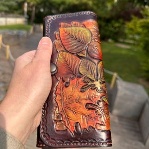 Cartera de mujer en piel marrón oscuro con estampado de hojas otoñales doradas grabadas a mano.