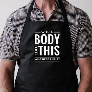 Puede incluir: Delantal negro con el texto blanco: "WITH A BODY LIKE THIS WHO NEEDS HAIR?". El delantal se lleva sobre una camisa a cuadros.