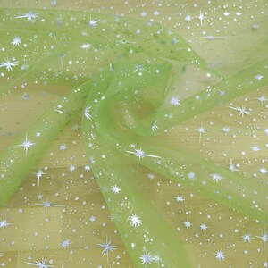 May include: Light green sheer fabric with a silver glitter star pattern. The fabric is draped and folded, showing the texture and sparkle of the material.