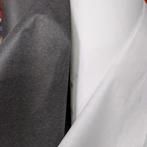 May include: Close-up of two rolls of fabric. One roll is black with a textured, dotted pattern. The other roll is white and smooth. The fabrics are likely used for sewing, crafting, or upholstery projects.