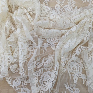 May include: Ivory white lace fabric with a floral pattern. The lace is delicate and sheer, with a soft, romantic feel.