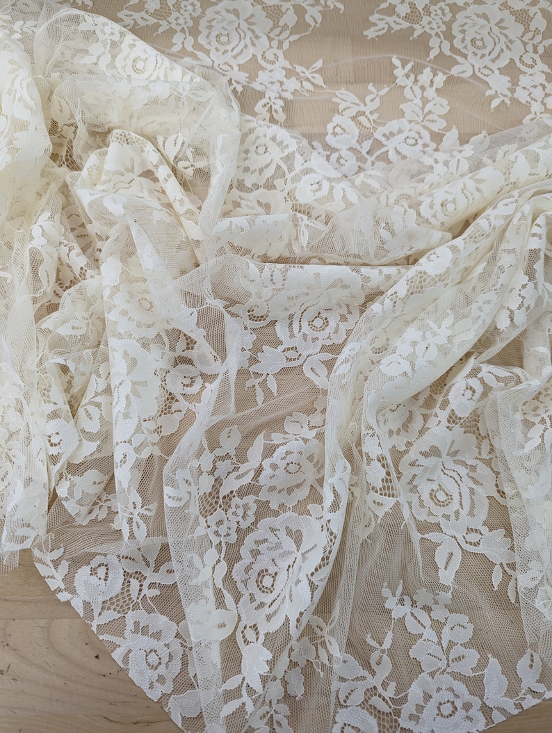 May include: Ivory white lace fabric with a floral pattern. The lace is delicate and sheer, with a soft, romantic feel.