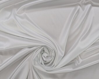 May include: A close-up shot of white satin fabric. The fabric is draped and folded, creating soft curves and shadows. The material has a smooth, shiny surface, reflecting light and giving a luxurious appearance. The fabric is gathered in a spiral pattern.