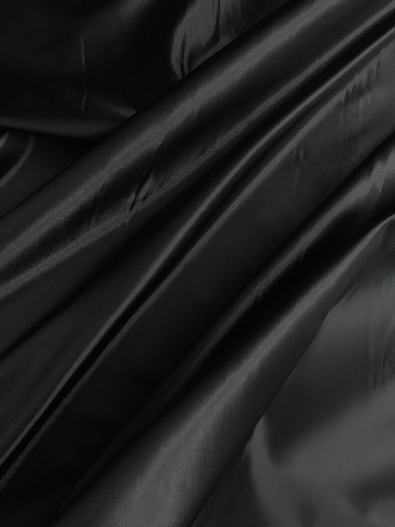 May include: Black satin fabric with a smooth, silky texture. The fabric is draped and folded, creating soft, flowing lines.