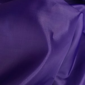 May include: A close-up of a smooth, purple fabric with a subtle sheen. The fabric is folded and draped, creating soft folds and curves.