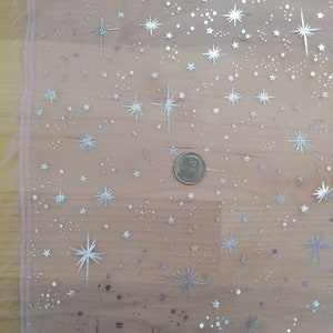 May include: A sheer pink fabric with a silver glitter star pattern. The fabric has a subtle shimmer and is perfect for crafting or decorating.