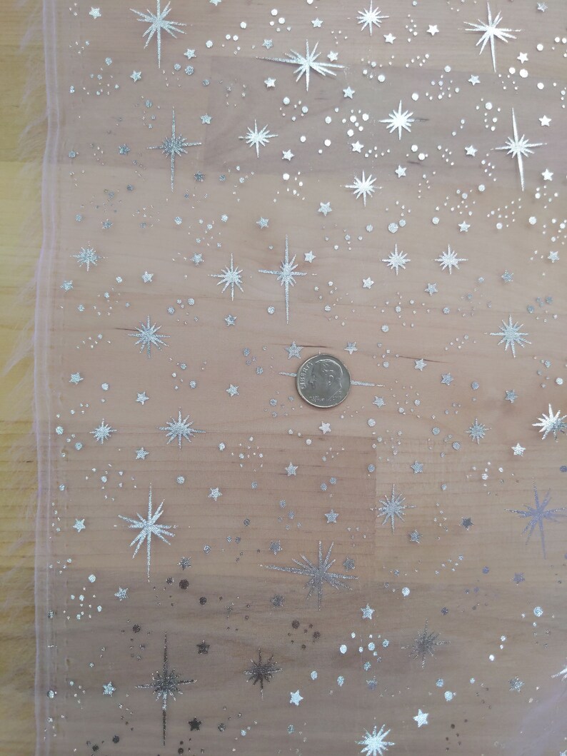 May include: A sheer pink fabric with a silver glitter star pattern. The fabric has a subtle shimmer and is perfect for crafting or decorating.