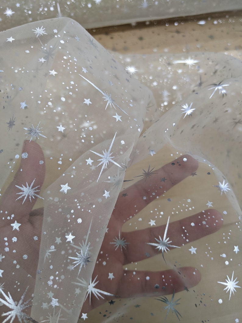 May include: White sheer fabric with a silver star pattern. The fabric is translucent and has a delicate, sparkly look.