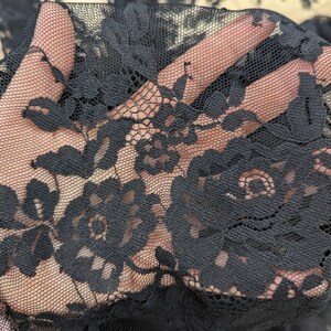 May include: Black lace fabric with a floral pattern. The lace is delicate and intricate, with a fine mesh background.