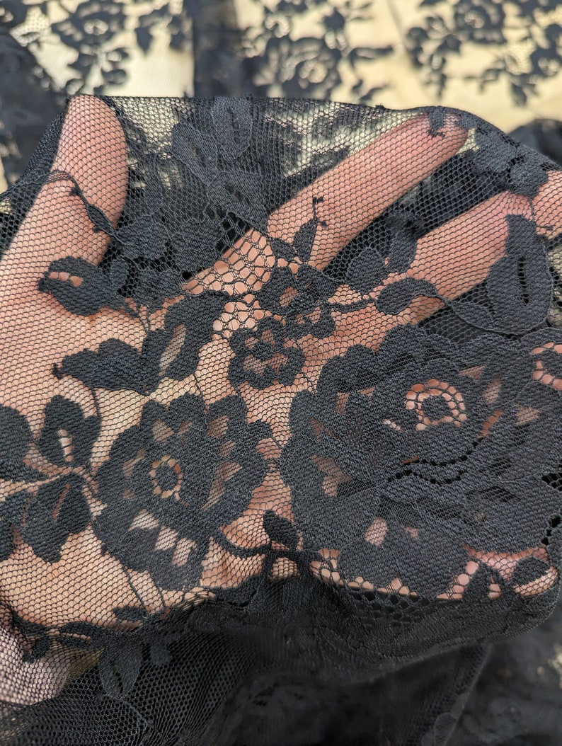 May include: Black lace fabric with a floral pattern. The lace is delicate and intricate, with a fine mesh background.