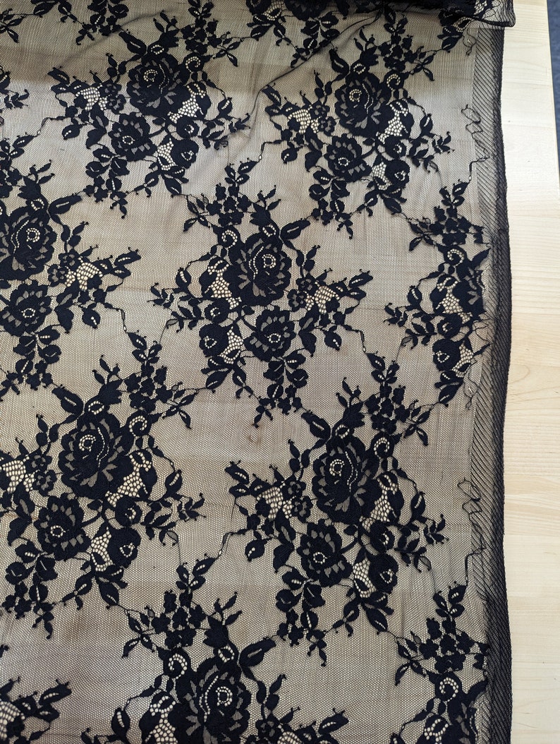 May include: Black lace fabric with a floral pattern. The lace is delicate and has a sheer appearance.