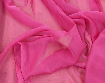 May include: A close-up of a bright pink sheer fabric with a slightly frayed edge. The fabric is draped and folded, creating soft, flowing lines.