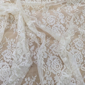May include: White floral lace fabric with a delicate pattern. The lace is sheer and has a soft, romantic feel.