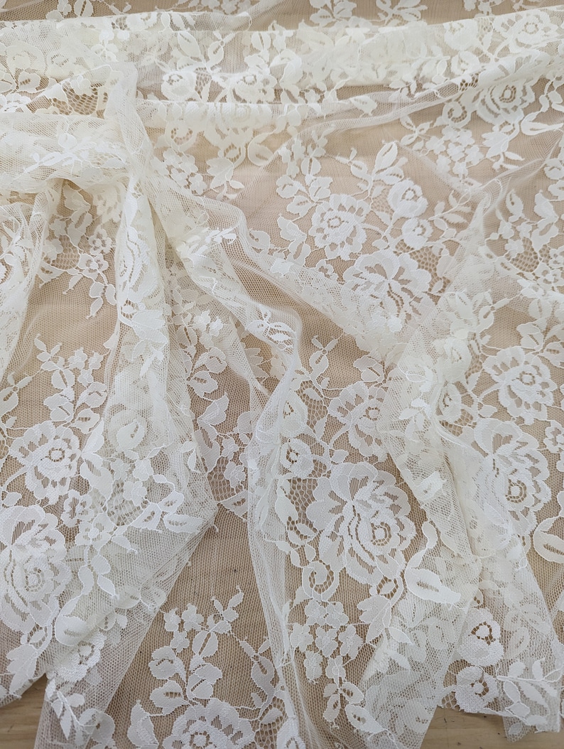 May include: White floral lace fabric with a delicate pattern. The lace is sheer and has a soft, romantic feel.