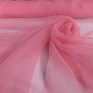 May include: A soft, pink sheer fabric with a delicate texture. The fabric is draped and folded, creating a flowing and elegant look.
