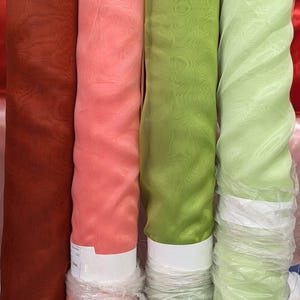 May include: Four rolls of sheer fabric in different colors: rust, pink, green, and light green. The fabric is rolled and wrapped in clear plastic.