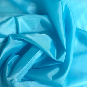 May include: A close-up of a light blue fabric with a smooth, silky texture. The fabric is folded and draped, showcasing its flowing nature.