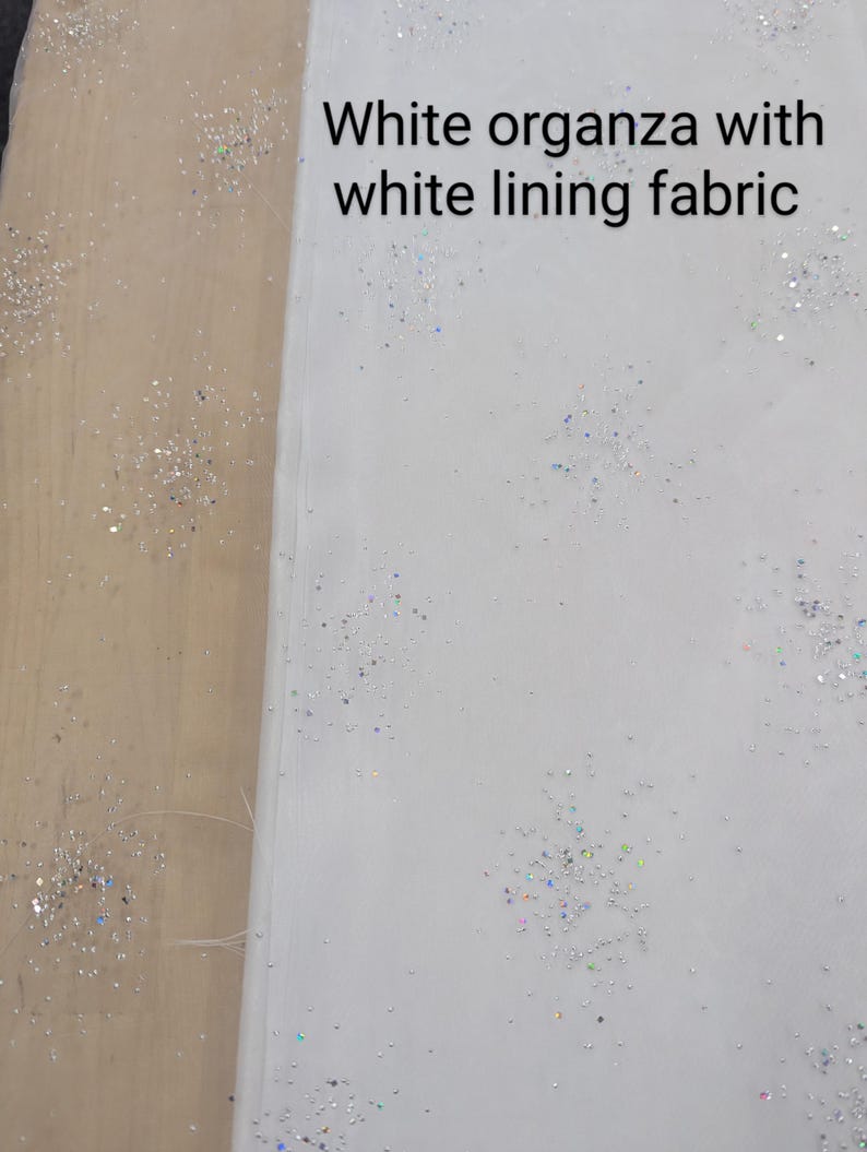 May include: White organza fabric with white lining, scattered with iridescent glitter. The text "White organza with white lining fabric" is visible on the fabric. This fabric is suitable for crafting and sewing projects.