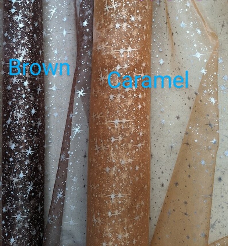 May include: Three rolls of sheer fabric with a silver star pattern. The fabric is brown, caramel, and a lighter brown color.
