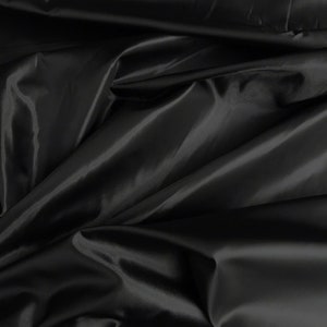 May include: Black satin fabric with a smooth, silky texture. The fabric is draped and folded, creating soft, flowing lines.