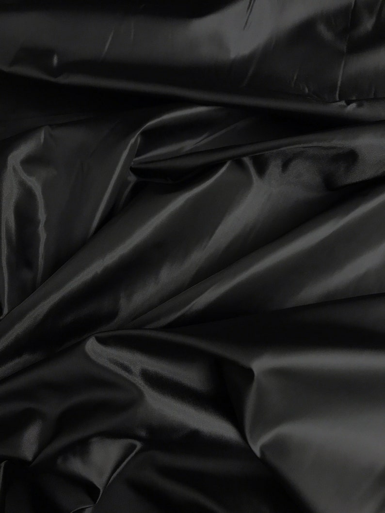May include: Black satin fabric with a smooth, silky texture. The fabric is draped and folded, creating soft, flowing lines.