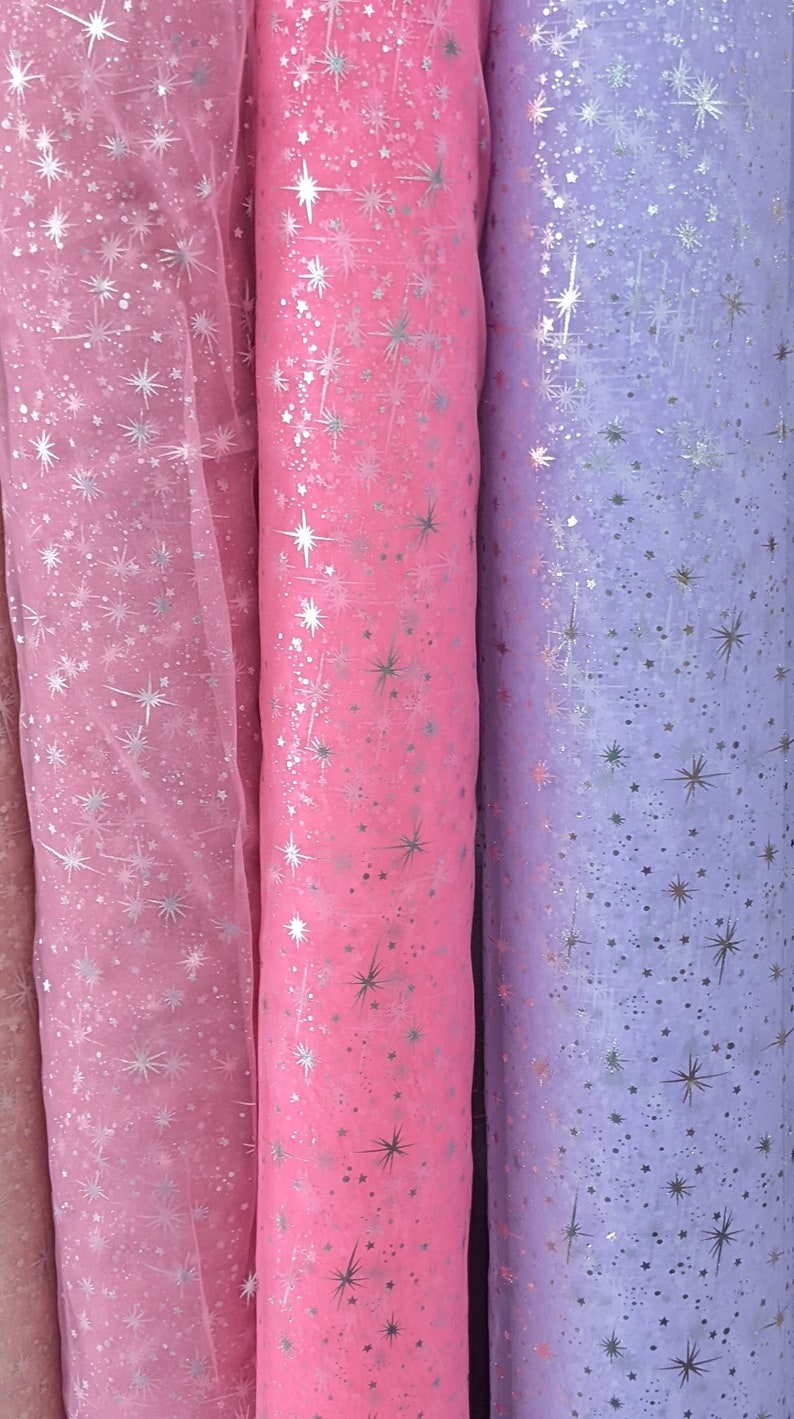 May include: Three rolls of sheer fabric with a silver star pattern. The fabric is pink, light pink, and lavender.