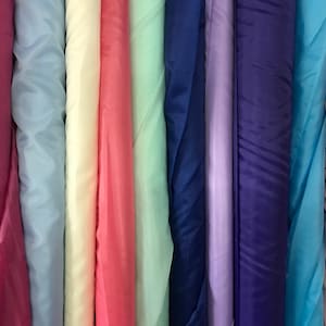 May include: A collection of fabric rolls in various colors, including pink, blue, light blue, cream, mint green, purple, navy blue, turquoise, and peach.
